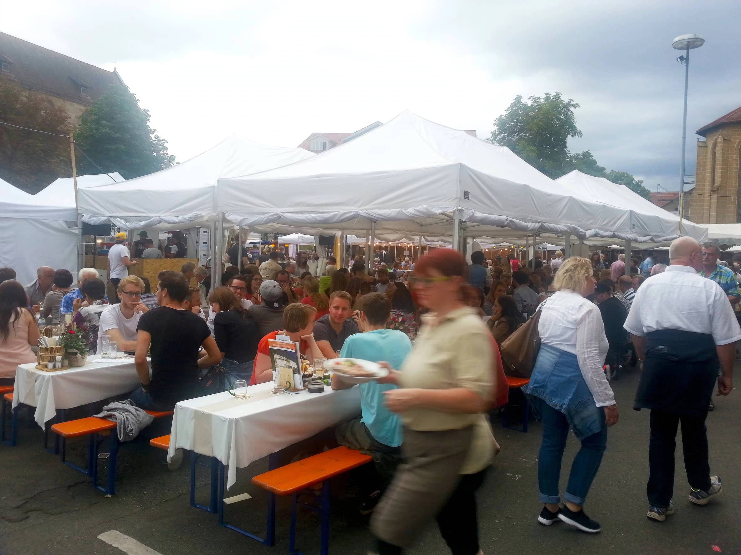 Faltzelte mieten für Stadtfeste: mehrere weiße MVL-TENT® Faltzelte aneinandergereiht mit Festzeltgarnituren und Gästen